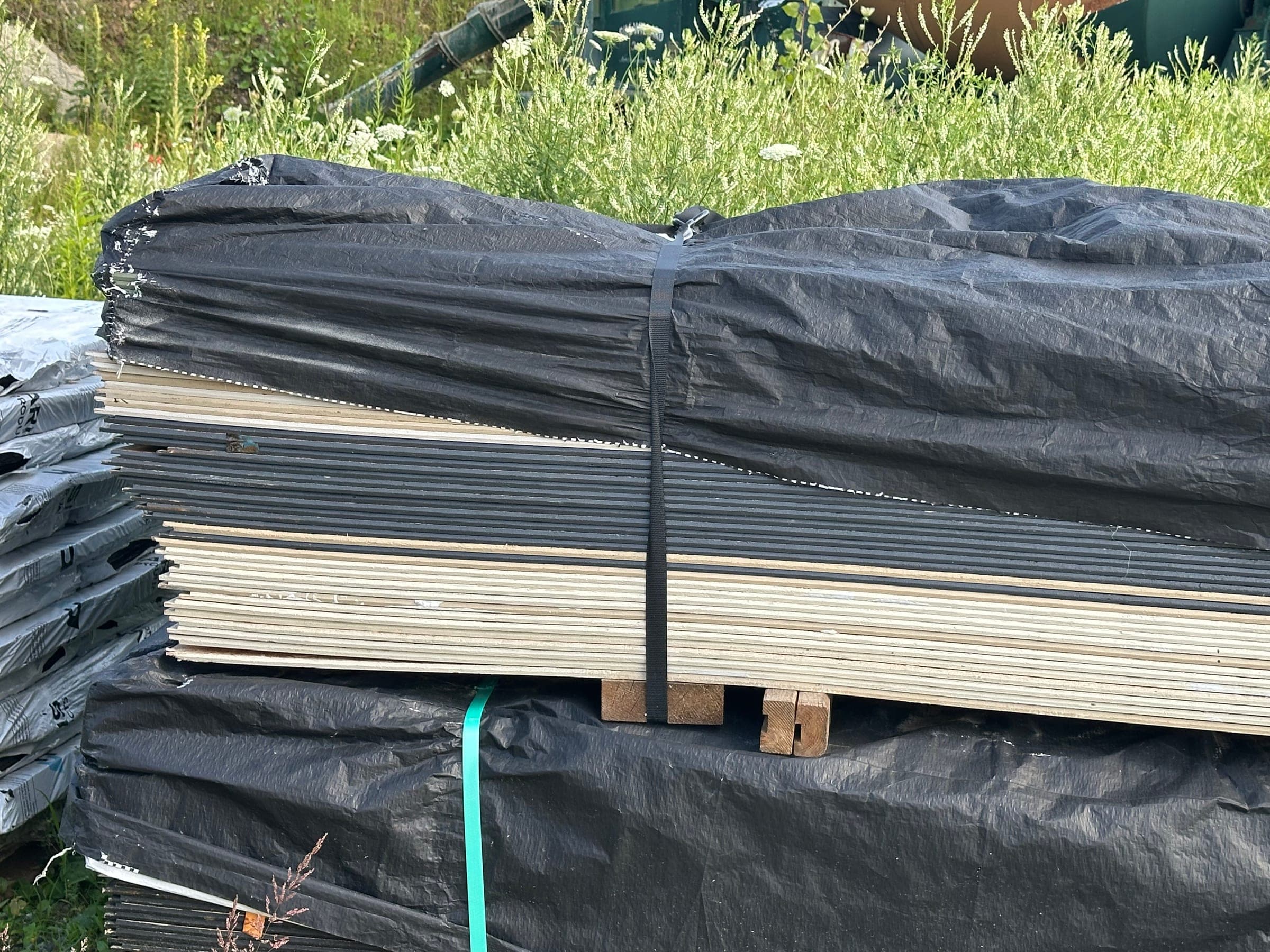 A banded pack of surplus siding in the yard, wrap open at the end to show cream and charcoal boards in the same unit
