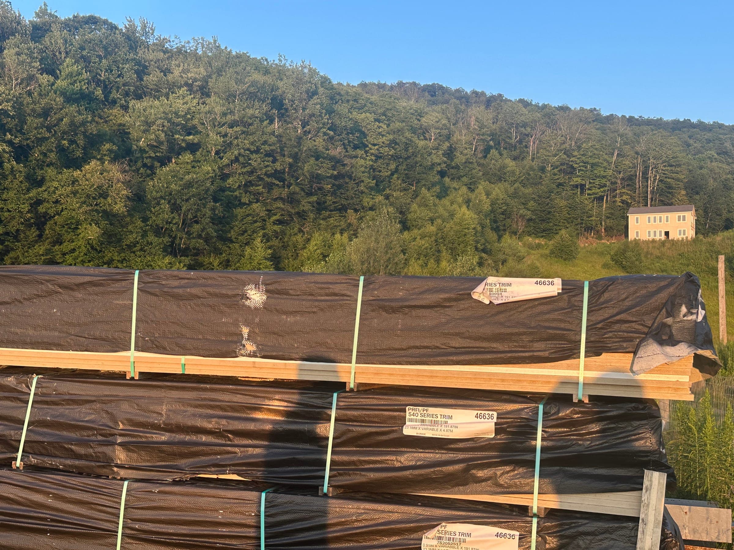 Banded trim under wrap in the Vermont yard, wooded hillside behind